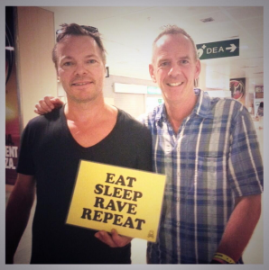 Fatboy Slim, con camisa de cuadros, y su amigo, Pete Tong, sosteniendo un cartel que reza "Come, duerme, ve de fiesta, repite". Foto: Twitter