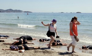 Dos turistas pasan por encima de los voluntarios de SOS Ayuda Refugiados Ibiza, que simulan su ahogamiento.